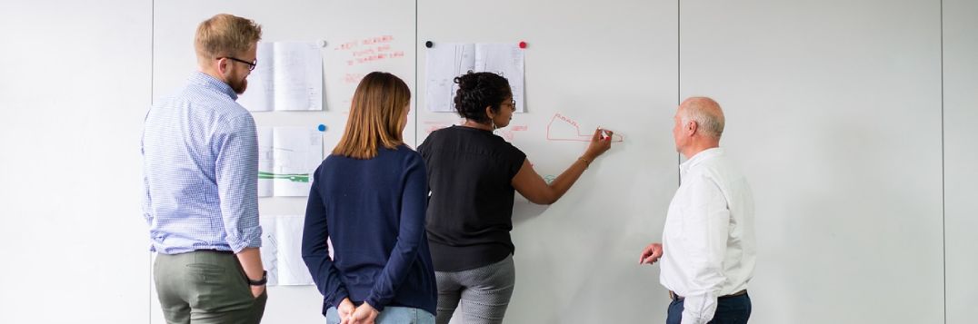 Photo de quatre personnes travaillant sur un tableau blanc